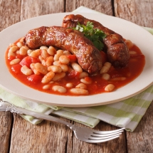 Pork Sausages With Beans And Cooked Tomatoes On A Plate Close-up