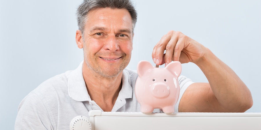 Portrait Of A Man Inserting Coin In Piggy Bank Kept On Radiator