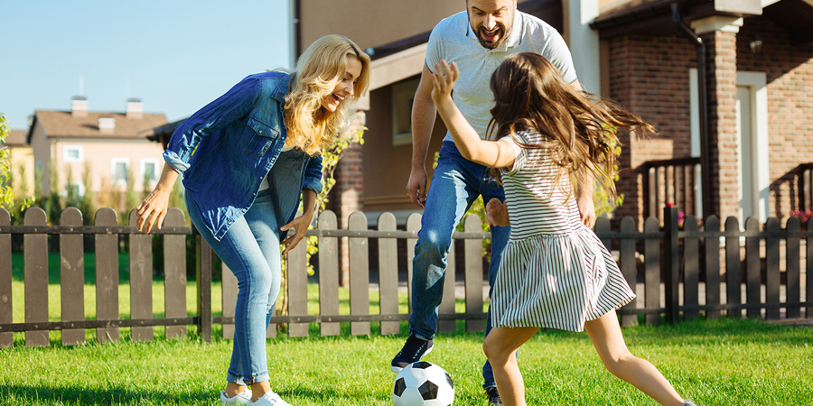 Mum, dad and daughter playing football in garden