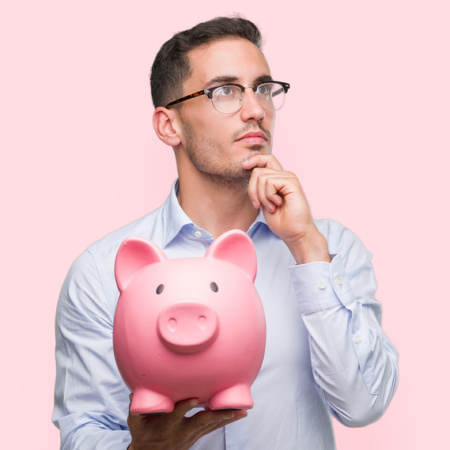 Handsome young man holding a piggy bank serious face thinking