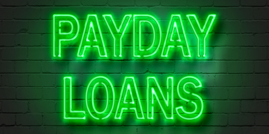 Green payday loans sign illuminated against brick wall