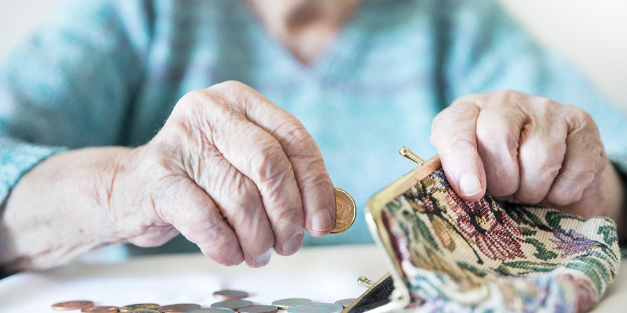 Detailed closeup photo of elderly womans hands counting remaining coins from pension in her wallet