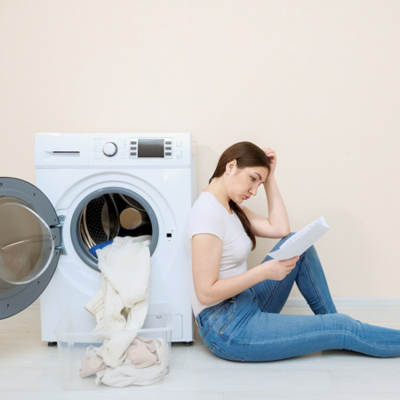 Young woman sitting against open washing machine