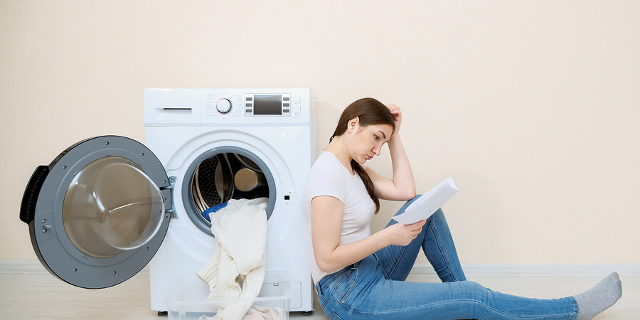 Young woman sitting against open washing machine