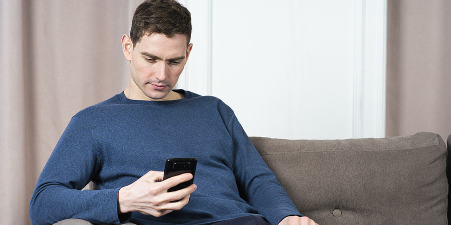 Young man reading text message on phone at home