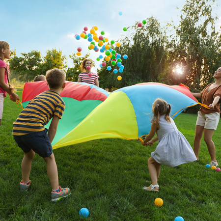 Group Of Children And Teachers Playing With Rainbow Parachute