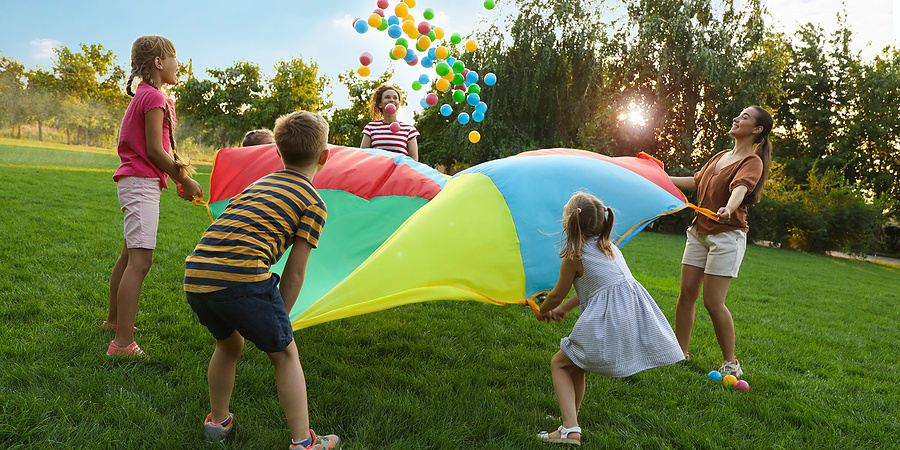 Group Of Children And Teachers Playing With Rainbow Parachute