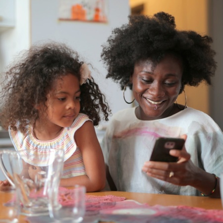 Woman looks happily at her phone with her daughter beside her
