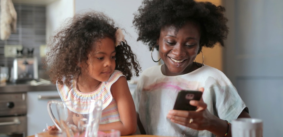 Woman looks happily at her phone with her daughter beside her