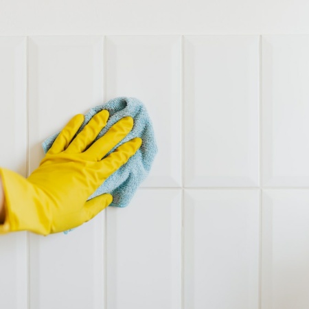 Hand in rubber glove cleaning bathroom tiles